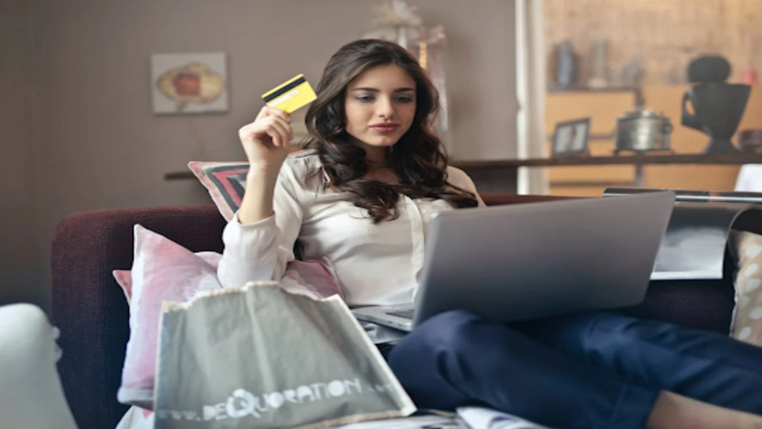 A woman holding her credit card with her computer on her lap.