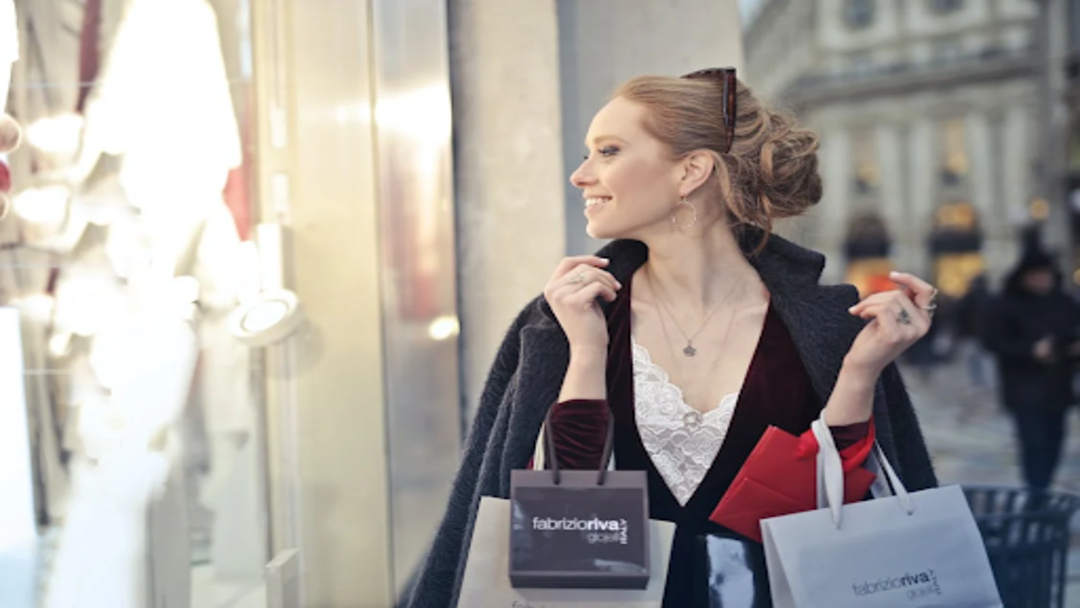 A woman window shopping while carrying several bags.