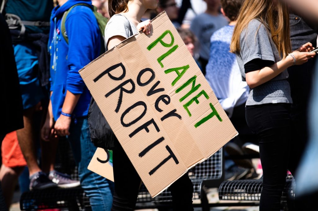 A person in a group of people holding a cardboard sign reading “Planet Over Profit.”