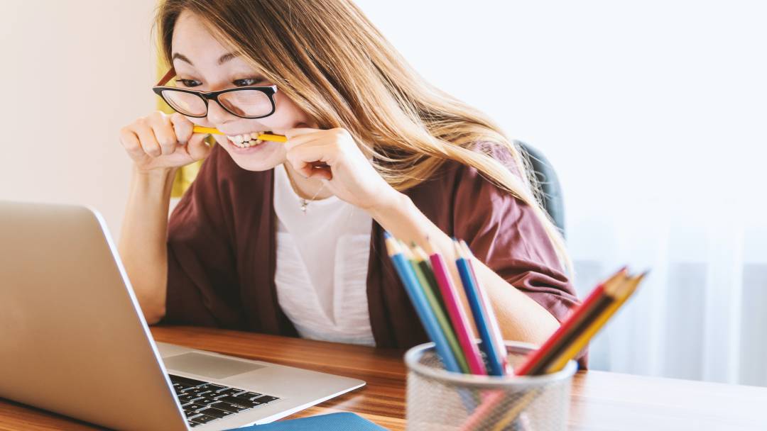 Woman biting a pencil while looking at her laptop