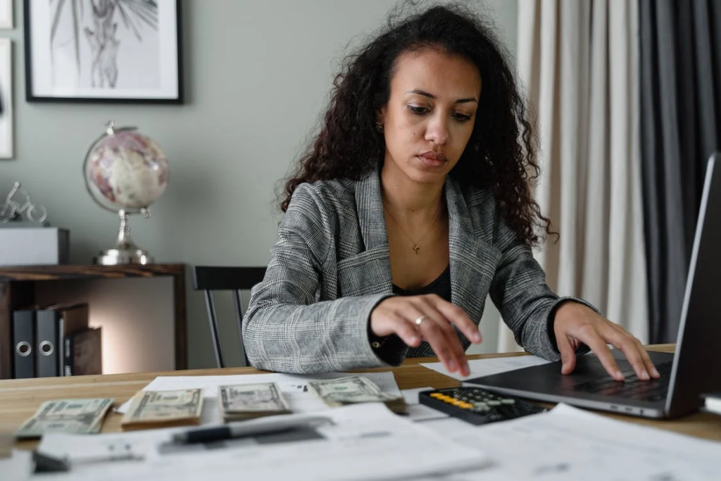 Woman using a laptop and calculator with money on the desk Image source